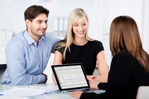 Couple Smiling While Looking At Financial Advisor At Desk